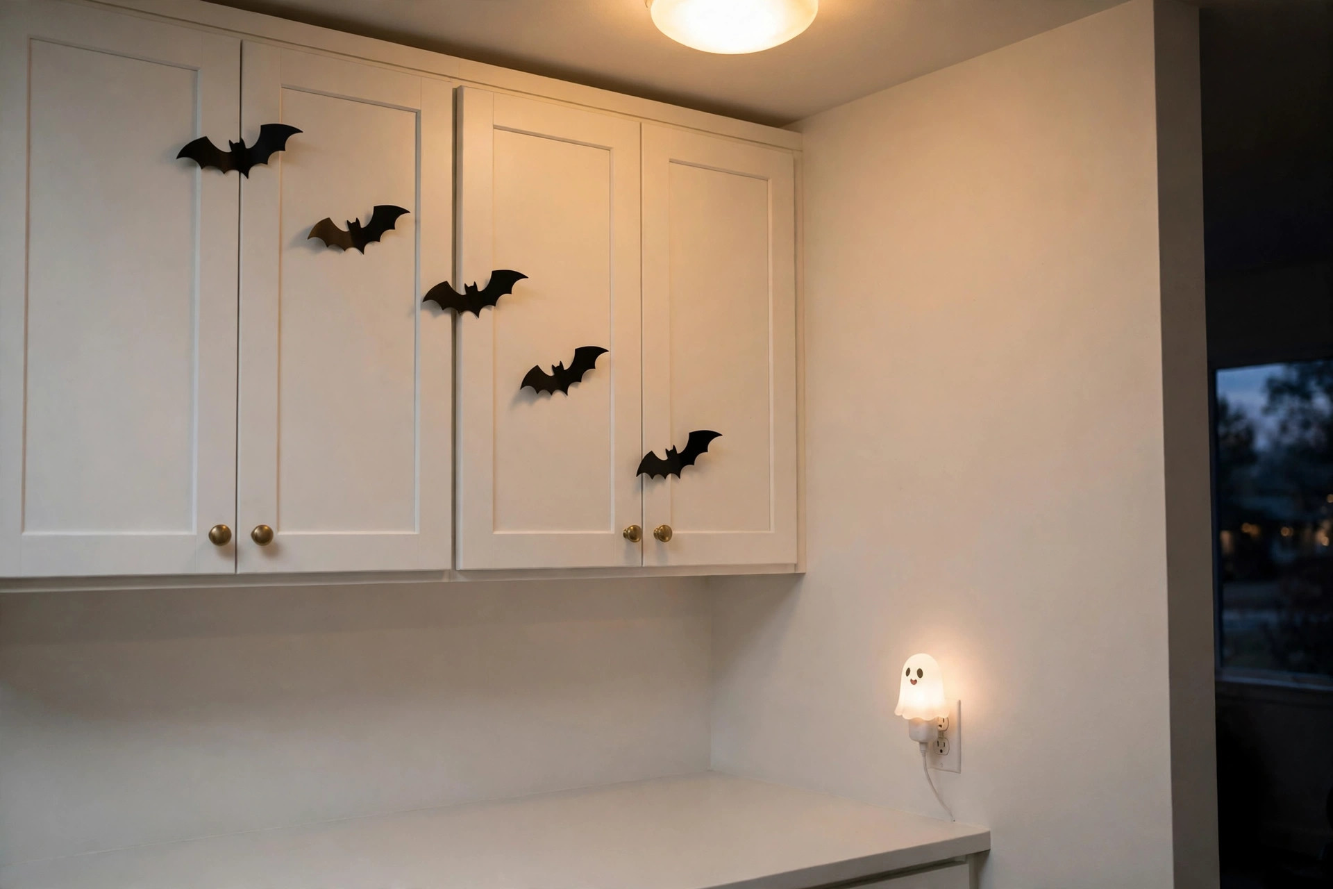 Cabinet doors with flat bat decals and a glowing ghost night light as halloween kitchen decor with an empty counter below