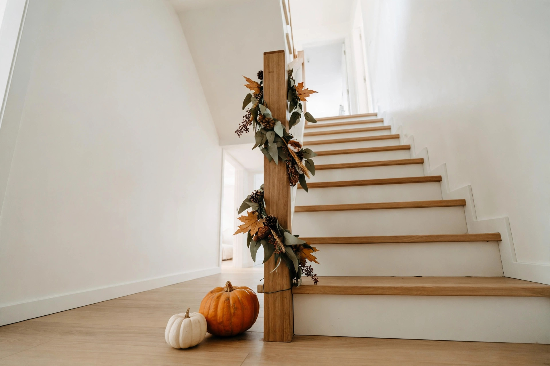 Newel post wrapped with a short fall garland and pumpkins at the base of a staircase decorated for halloween