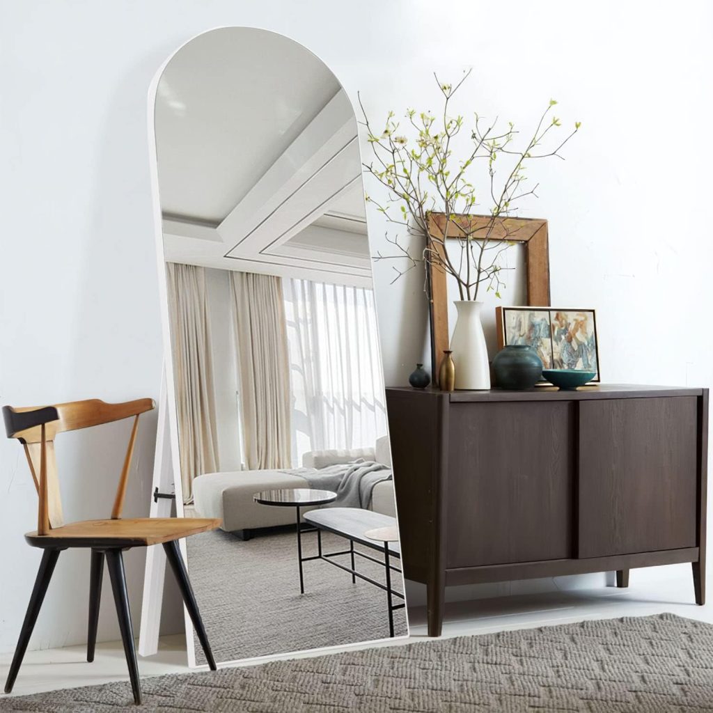 NeuType arched full length mirror on its stand beside a dark wood cabinet in a bright room