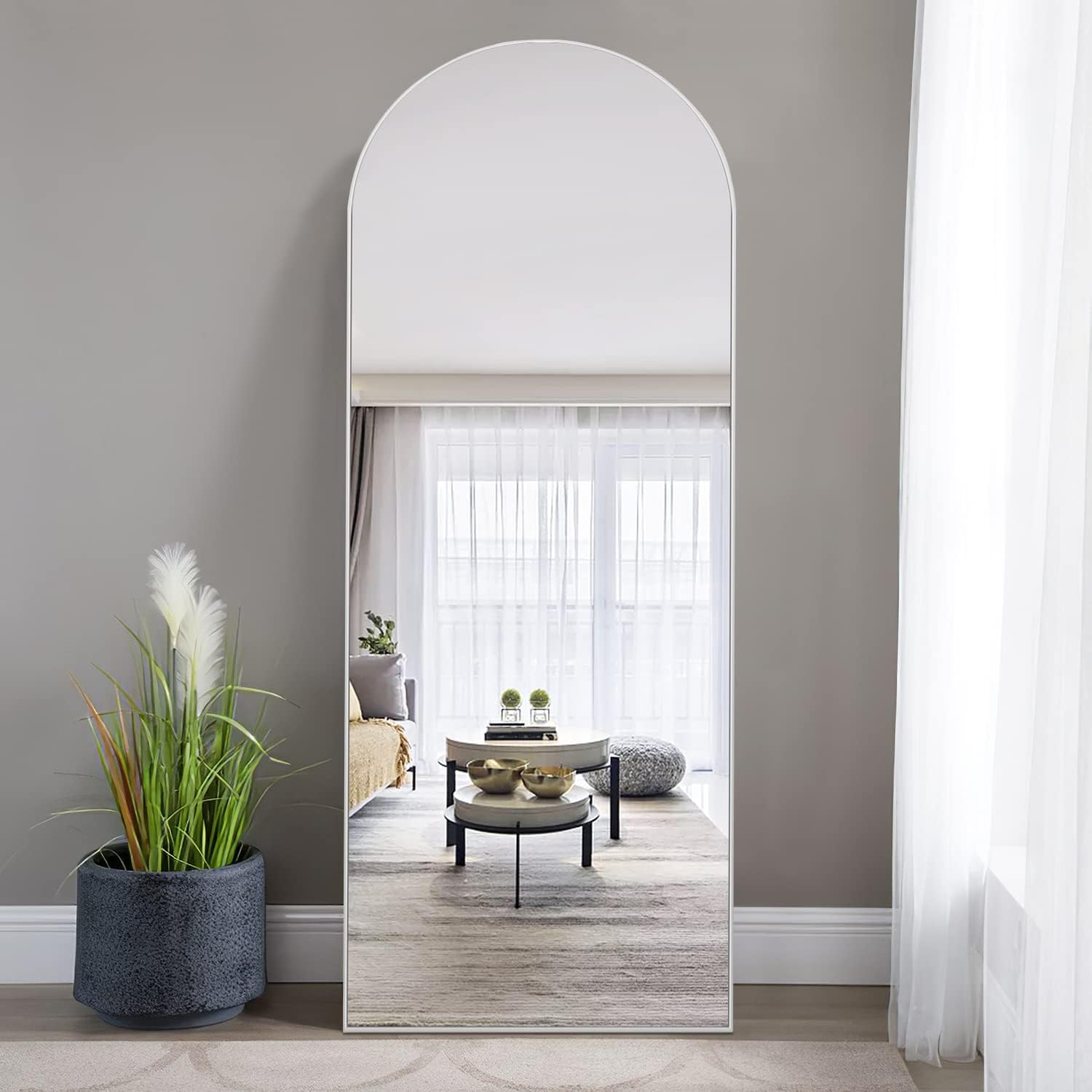 NeuType 65 by 22 inch arched full length mirror with thin white metal frame leaning against a grey living room wall